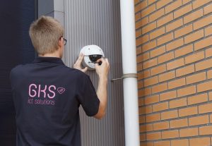 Een afbeelding van een sfeerbeeld op gks.nl waarop een man een bewakingscamera op een pand installeert.