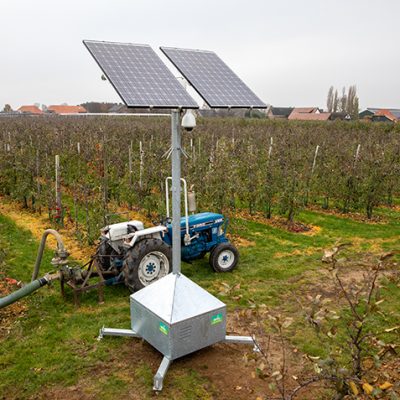 Sfeerbeeld van objectbeveiliging met een mobiele cameramast in een boomgaard. Achter de mast staat een blauwe tractor die is aangesloten op de waterpompinstallatie.