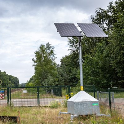 Sfeerbeeld van een mobiele cameramast die op de groenstrook langs het spoor staat bij een onbewaakte spoorwegovergang.