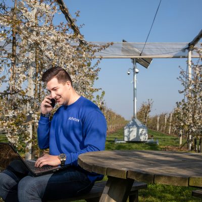 Adhetec medewerker bij een mobiele cameramast op een onbewaakt terrein. Sfeerbeeld van een mobiele cameramast en een monteur in een boomgaard.