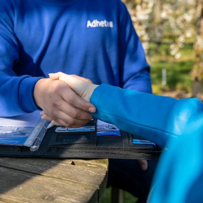Adhetec helpt u met slimme camerasystemen Sfeerbeeld van een man en een vrouw in het blauw gekleed die elkaar de hand schudden.